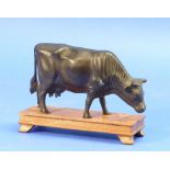 A oriental bronze model of a Cow, standing, on wooden base, 4¾in (12cm) high.