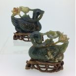 A pair of early 20thC Chinese jade Ducks, each holding a lily in its beak, on wood stands, with