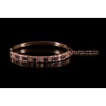 An antique 15ct rose coloured gold diamond and blue stone bangle, c.1900, the top set with seven old