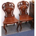 A good pair of Victorian mahogany hall chairs, with carved backs, solid seats and raised on cabriole