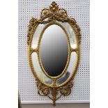 A late 19th / early 20th Century gilt framed oval mirror, carved and swagged pediment etc, the