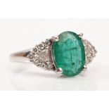 A platinum, emerald and diamond ring The oval-cut emerald, between two trilliant and brilliant-cut