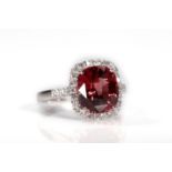 A garnet and diamond cluster ring The cushion-shaped garnet, within a surround of brilliant-cut