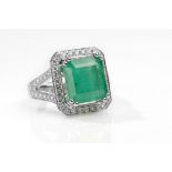An emerald and diamond dress ring The step-cut emerald, to a surround and bifurcated shoulders set