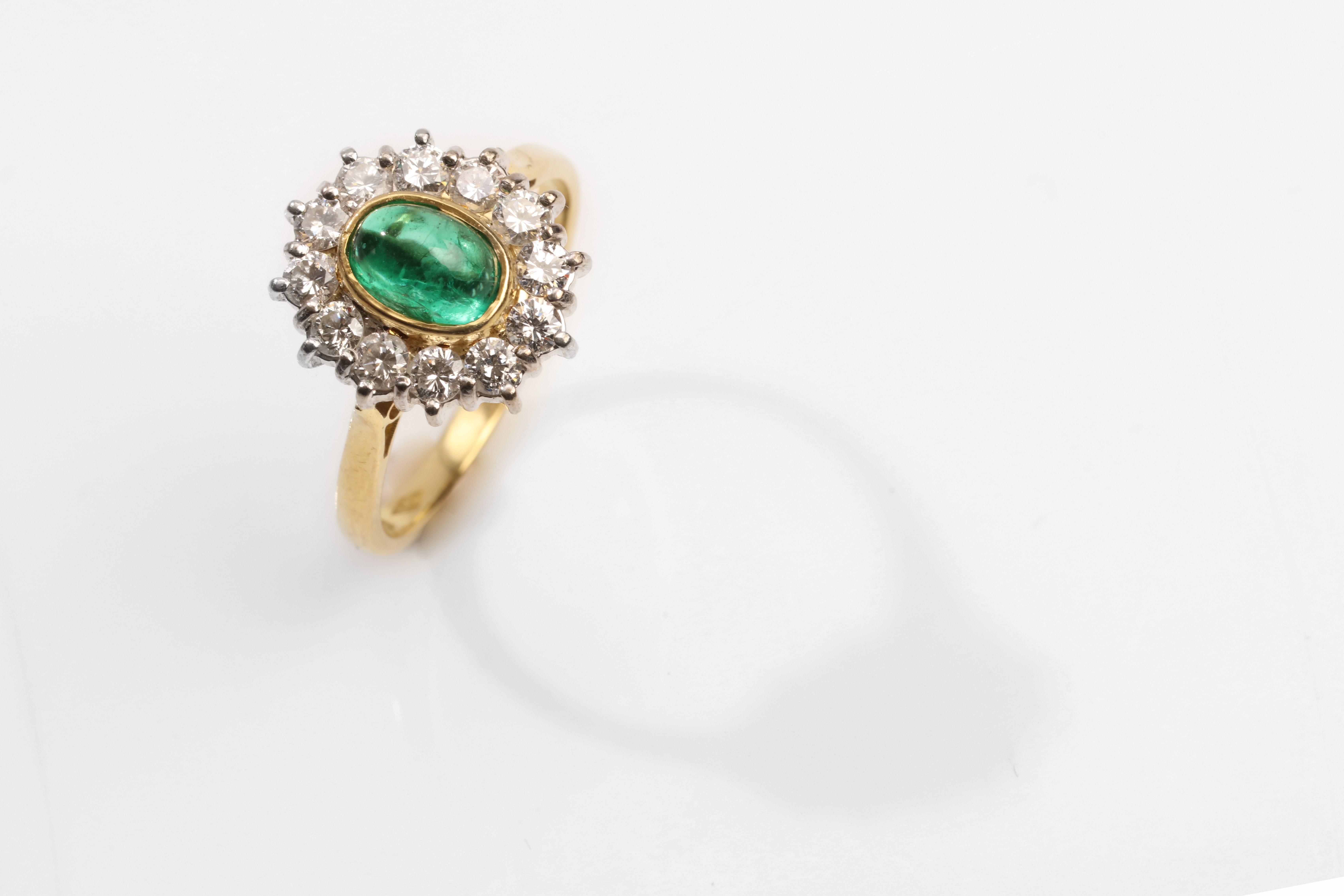 An emerald and diamond cluster ring, 1989 The collet-set oval-cut cabochon emerald, within a