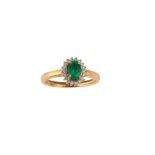 An emerald and diamond cluster ring The oval-cut emerald, in a four-claw setting, within a