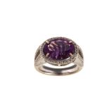 An amethyst and diamond ring The oval mixed-cut amethyst, within a halo surround of brilliant-cut