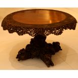 A 19th Century Burmese carved hardwood circular table, the tilt top with pierced rim on a