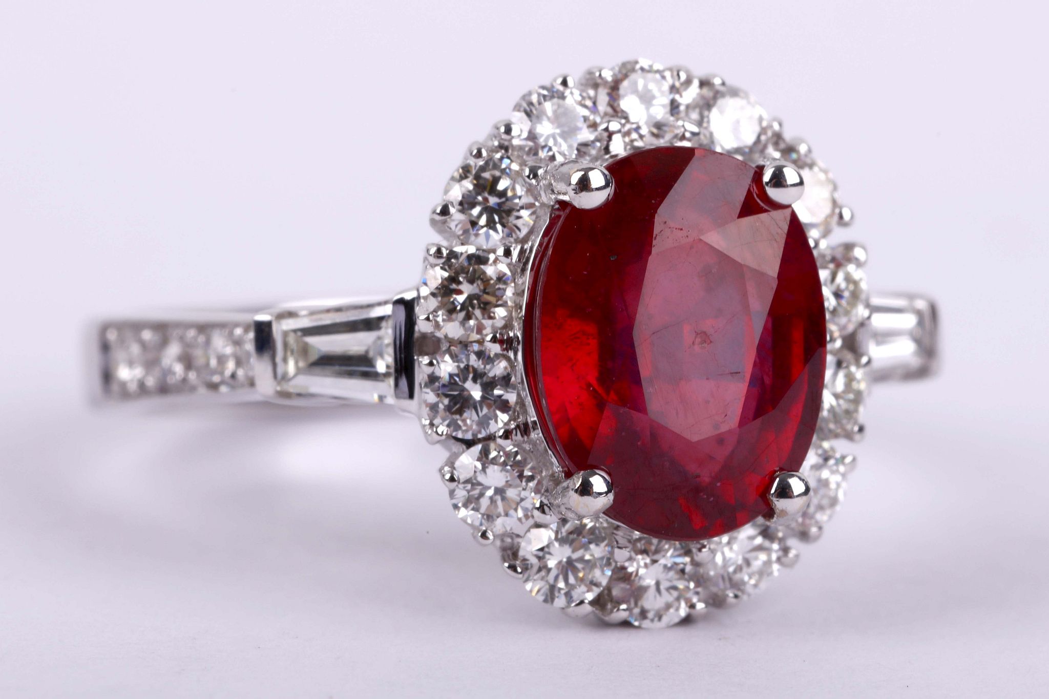 A glass filed ruby and diamond ring, The oval-cut glass filled ruby, within a surround of