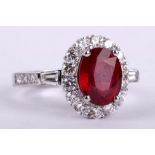 A glass filed ruby and diamond ring, The oval-cut glass filled ruby, within a surround of