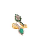 An emerald and diamond dress ring Of crossover design, the pear-shaped emerald terminal within a