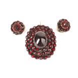 A garnet brooch and earclips, late 19th century The oval brooch of tiered design, centrally set with