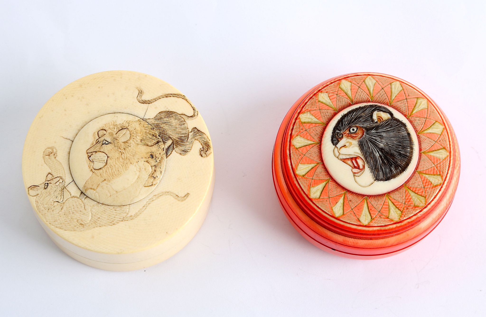 Two Japanese Meiji period circular ivory boxes. One is stained red and carved with animals head to