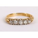 An 18K yellow gold and diamond set graduated five stone ring with scroll gallery.