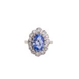 A sapphire and diamond cluster ring The oval-cut sapphire, within a brilliant-cut diamond