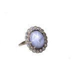 A star sapphire and diamond cluster ring The oval cabochon star sapphire, within a scalloped