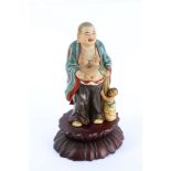 A Chinese porcelain model of a Buddha, standing open chested, holding a bag from which emerges a