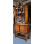A Queen Anne revival walnut display cabinet, with arched top over glazed door and cupboard base,