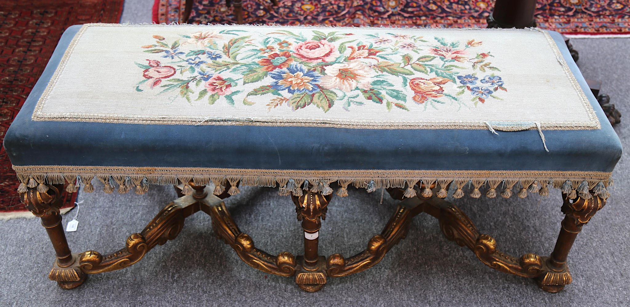 A William and Mary style giltwood long stool, with needlework upholstered seat on stretchered legs.