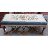 A William and Mary style giltwood long stool, with needlework upholstered seat on stretchered legs.