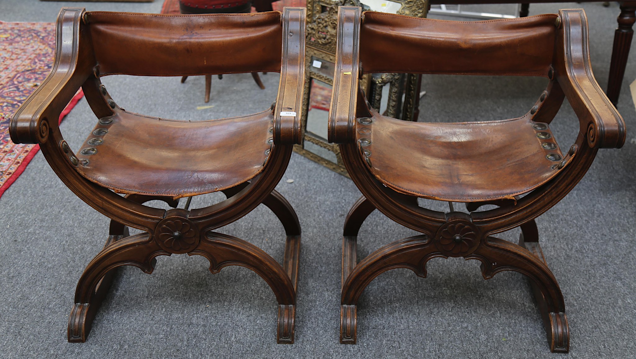 A pair of 18th Century style, Italian walnut X frame elbow chairs with tan leather backs and seats.