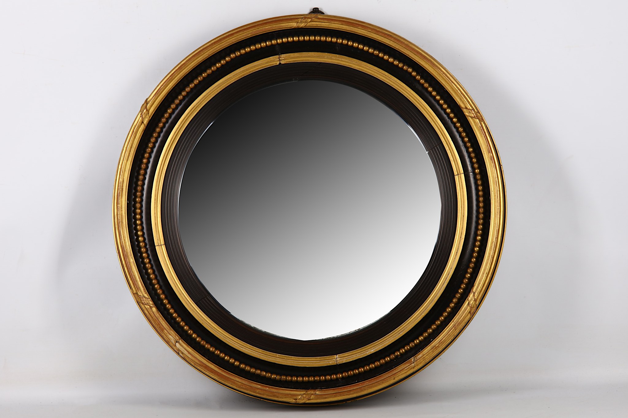 A Regency convex mirror, early 19th Century, in a moulded ebonised and parcel gilt circular frame,