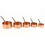 A graduated set of five copper saucepans with iron handles.