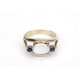 A moonstone and sapphire ring, The oval cabochon moonstone, between circular-cut sapphires,