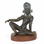 An Indian bronze figure of a seated deity wearing headdress, on an oval wood plinth,