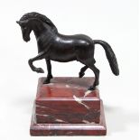 A bronze figure of a pacing stallion on a polished red marble plinth,