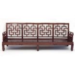 A pair of Chinese hardwood settees, each with four panelled lattice style backs and arms,