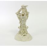 A Belleek spill vase, modelled as a flower encrusted stump surmounted by a bird, black printed mark,