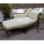 A Victorian walnut framed chaise longue with carved scrolling legs on brass castors,