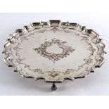 A large silver plated salver with pie crust border and engraved decoration, on three scroll feet,