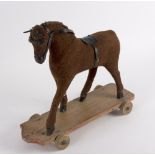 A child's pull-a-long horse, material covered and with leather harness, on a four wheeled pine base,