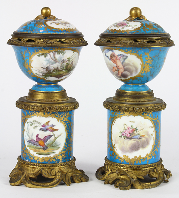 Pair of Sevres style cylindrical lidded urns, each having floral reserves and accented with gilt