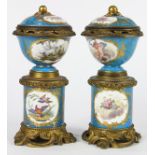 Pair of Sevres style cylindrical lidded urns, each having floral reserves and accented with gilt