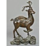 Chinese patinated bronze deer, standing on three legs on a rocky plinth, clasping a sprig in its