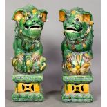 Pair of Chinese glazed ceramic fu-lions, of green and yellow hues on a rectangular plinth, 13.75"h