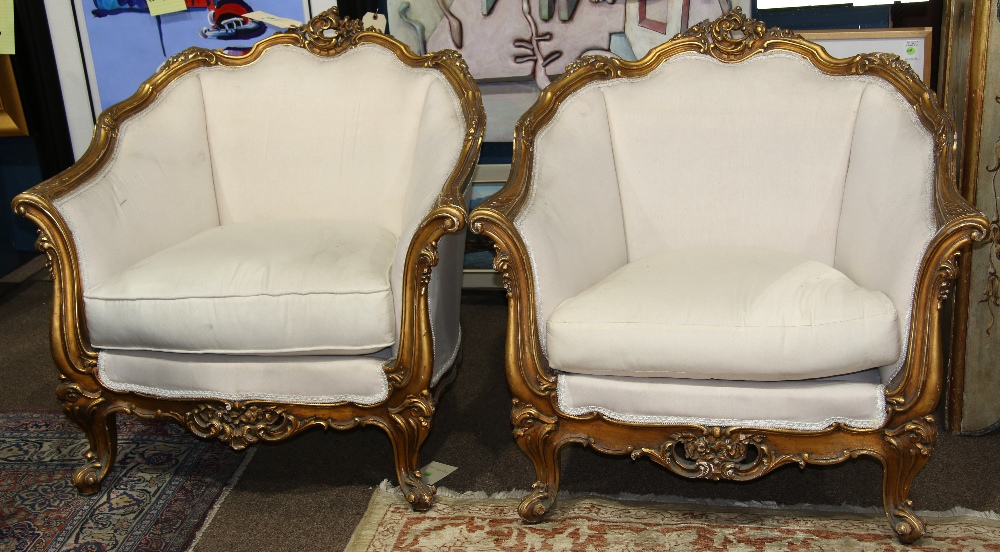 (lot of 2) Louis XV style giltwood bergeres, each having a floral carved crest, above a cream