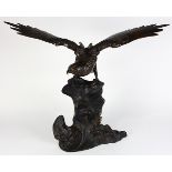 Japanese copper alloy sculpture of a hawk, with wings expanded and perched on the separate rock form