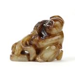 Chinese hardstone carving, of a seated child pulling a sprig of peach, with brown patches in