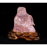 Chinese rose quartz figure, of bodhidharma seated in laliasana holding a fly whisk, with wood stand,