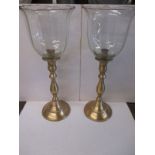 A pair of brass candlesticks with upturned glass shades