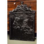 Cast iron fireback depicting two figures with a cherub crest above, a wrought iron fire basket and