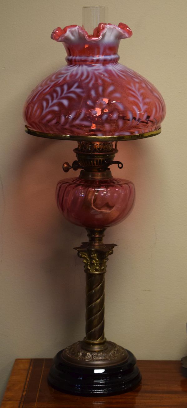 Early 20th Century oil lamp having a pink glass reservoir, brass column and standing on a black