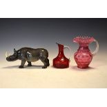 Melba Ware figure of a rhinoceros together with a cranberry glass jug and a ruby glass carafe