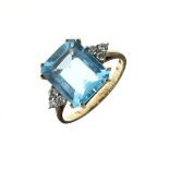 Blue topaz and diamond 9ct gold ring, the step cut stone with a trio of diamonds to each shoulder,