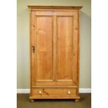 Natural pine wardrobe fitted a panelled door with one drawer below and standing on bun feet
