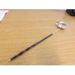 A silver metal punch ladle with pouring lip and twisted whale bone handle set with silver coin dated